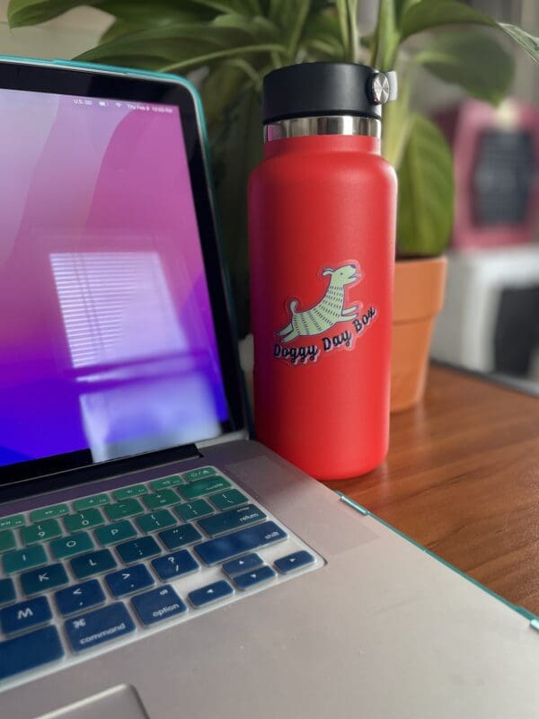 A red thermos sitting next to a laptop.