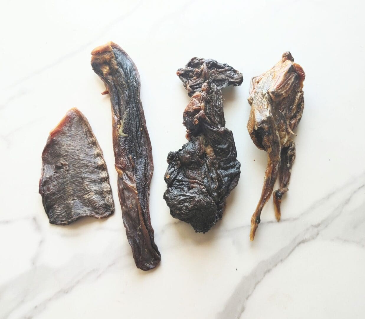 Four dried meat treats on white marble.